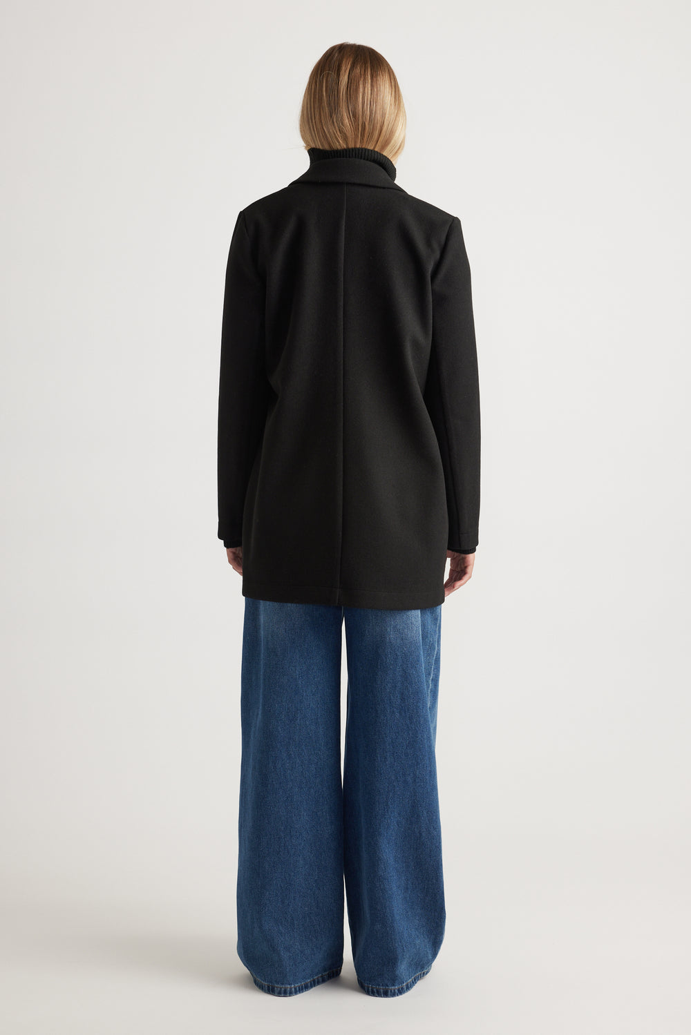 Back view of woman wearing a black mid-length felt coat paired with wide-leg blue denim jeans for a casual look