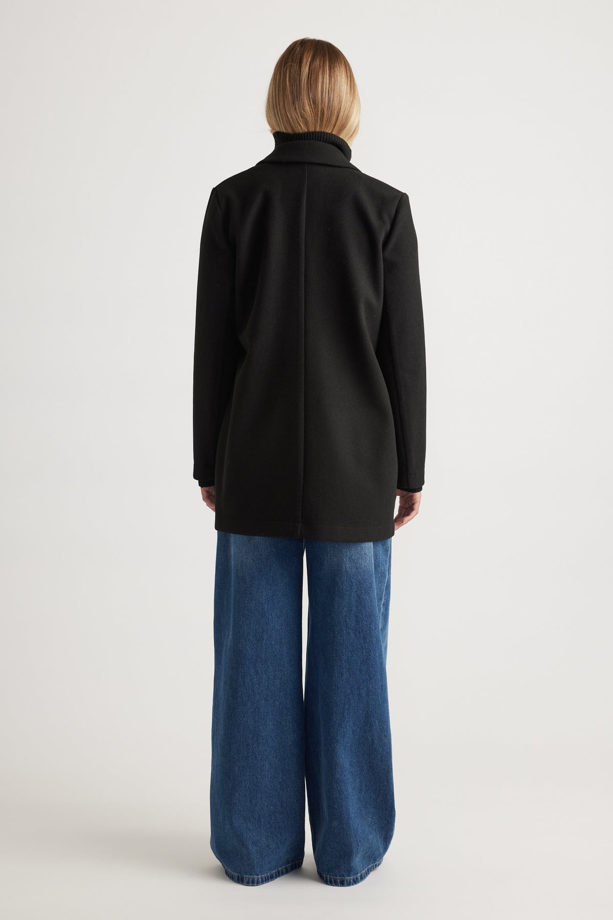 Back view of woman wearing a black mid-length felt coat paired with wide-leg blue denim jeans for a casual look