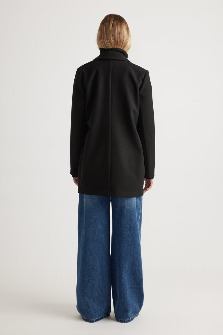 Back view of woman wearing a black mid-length felt coat paired with wide-leg blue denim jeans for a casual look