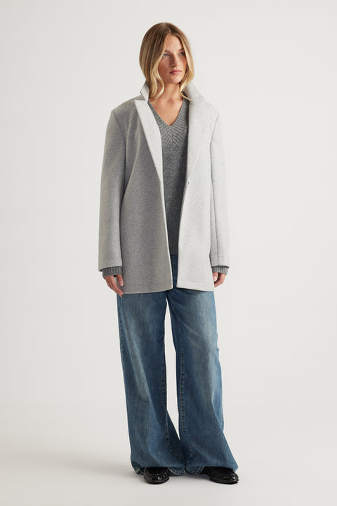 Woman wearing a light grey mid-length coat layered over a grey knit sweater and wide-leg blue denim jeans for a casual look