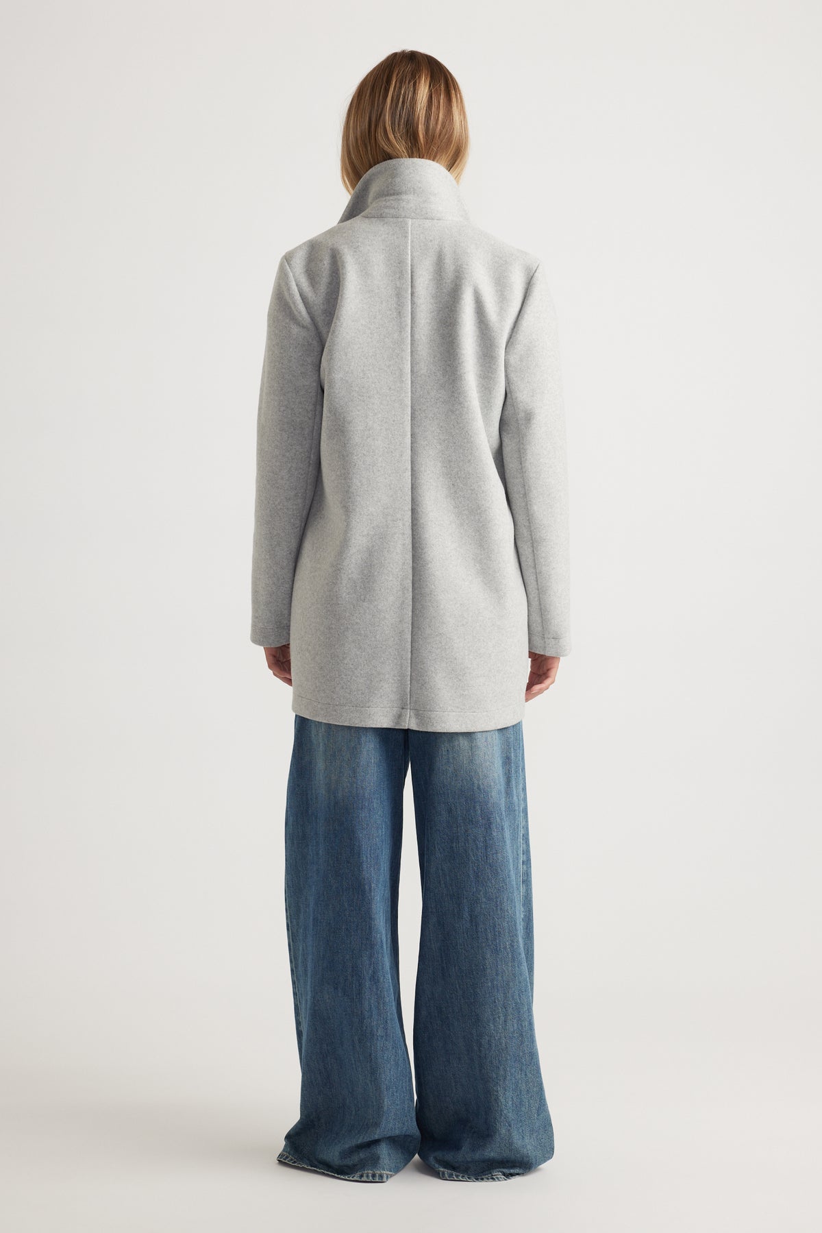 Woman wearing a light grey mid length coat paired with wide-leg blue denim jeans for a relaxed look