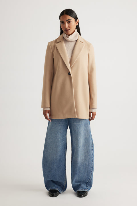 Woman wearing a soft camel mid length coat layered over a beige turtleneck paired with wide-leg denim jeans for a modern look