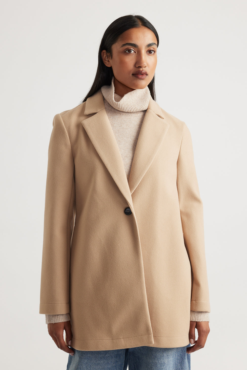 Soft camel mid-length coat with single button and tailored lapels layered over a light beige turtleneck sweater