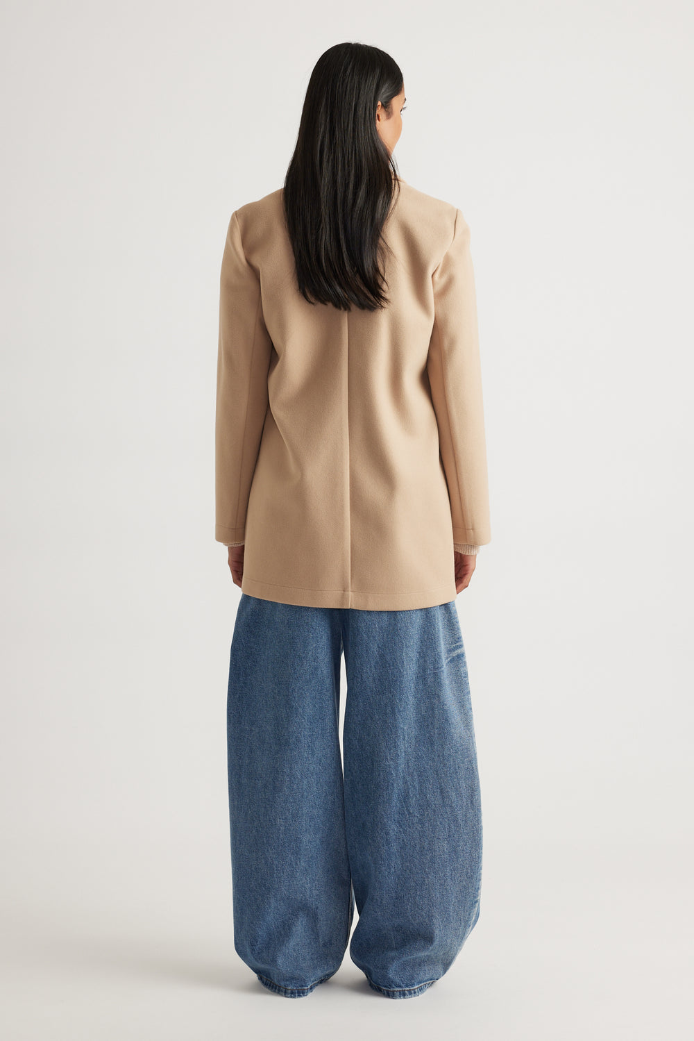 Woman wearing a soft camel mid-length coat with structured shoulders paired with loose-fitting wide-leg denim pants
