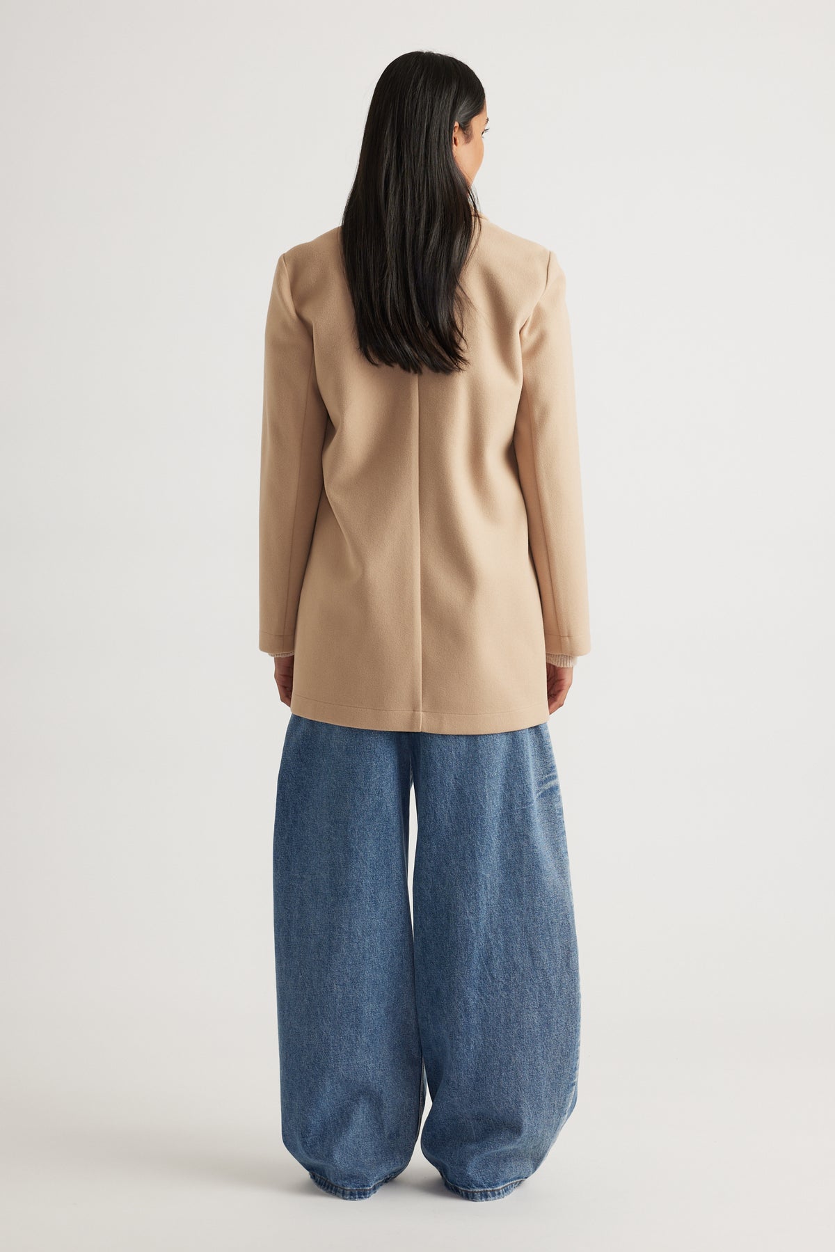 Woman wearing a soft camel mid-length coat with structured shoulders paired with loose-fitting wide-leg denim pants