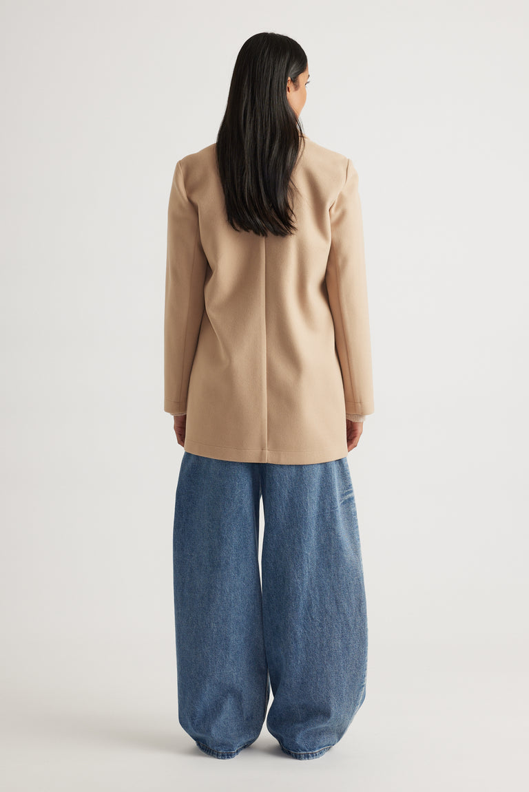 Woman wearing a soft camel mid-length coat with structured shoulders paired with loose-fitting wide-leg denim pants