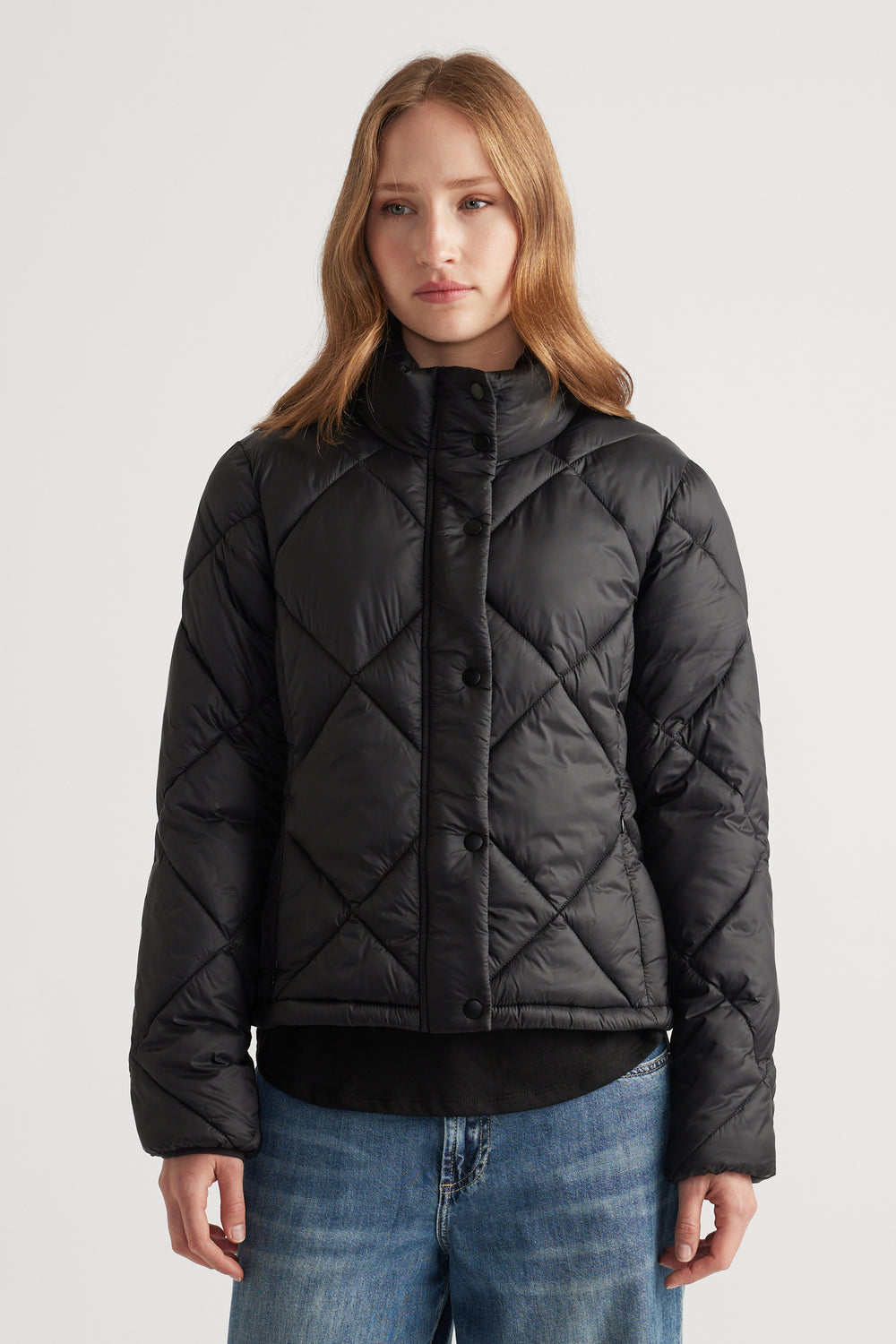 Woman wearing a black quilted short puffer jacket with a high collar paired with relaxed blue denim jeans