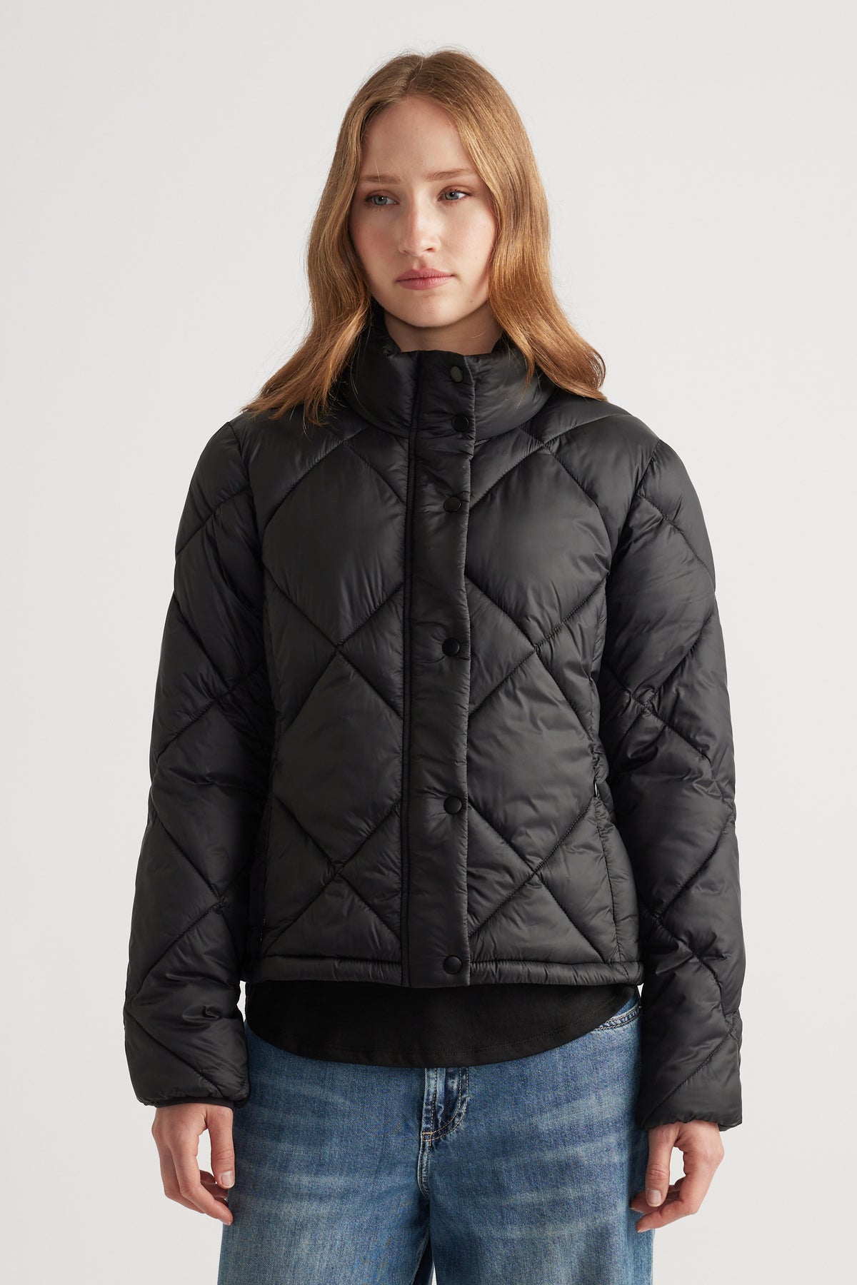 Woman wearing a black quilted short puffer jacket with a high collar paired with relaxed blue denim jeans