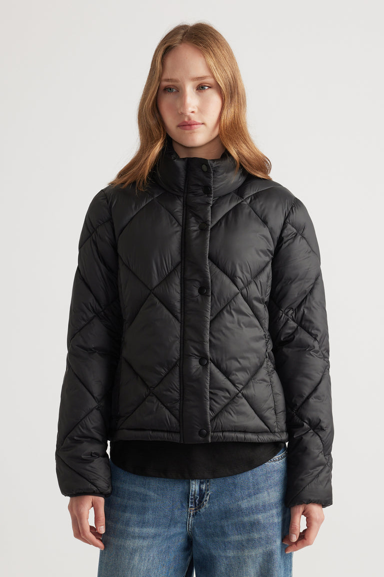 Woman wearing a black quilted short puffer jacket with a high collar paired with relaxed blue denim jeans