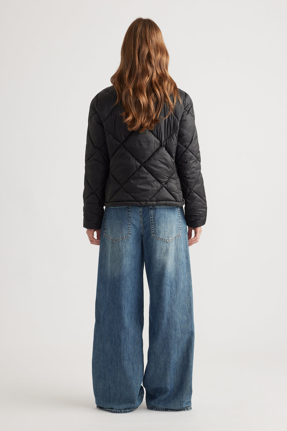 Woman shown from behind wearing a black quilted short puffer jacket with wide-leg blue jeans