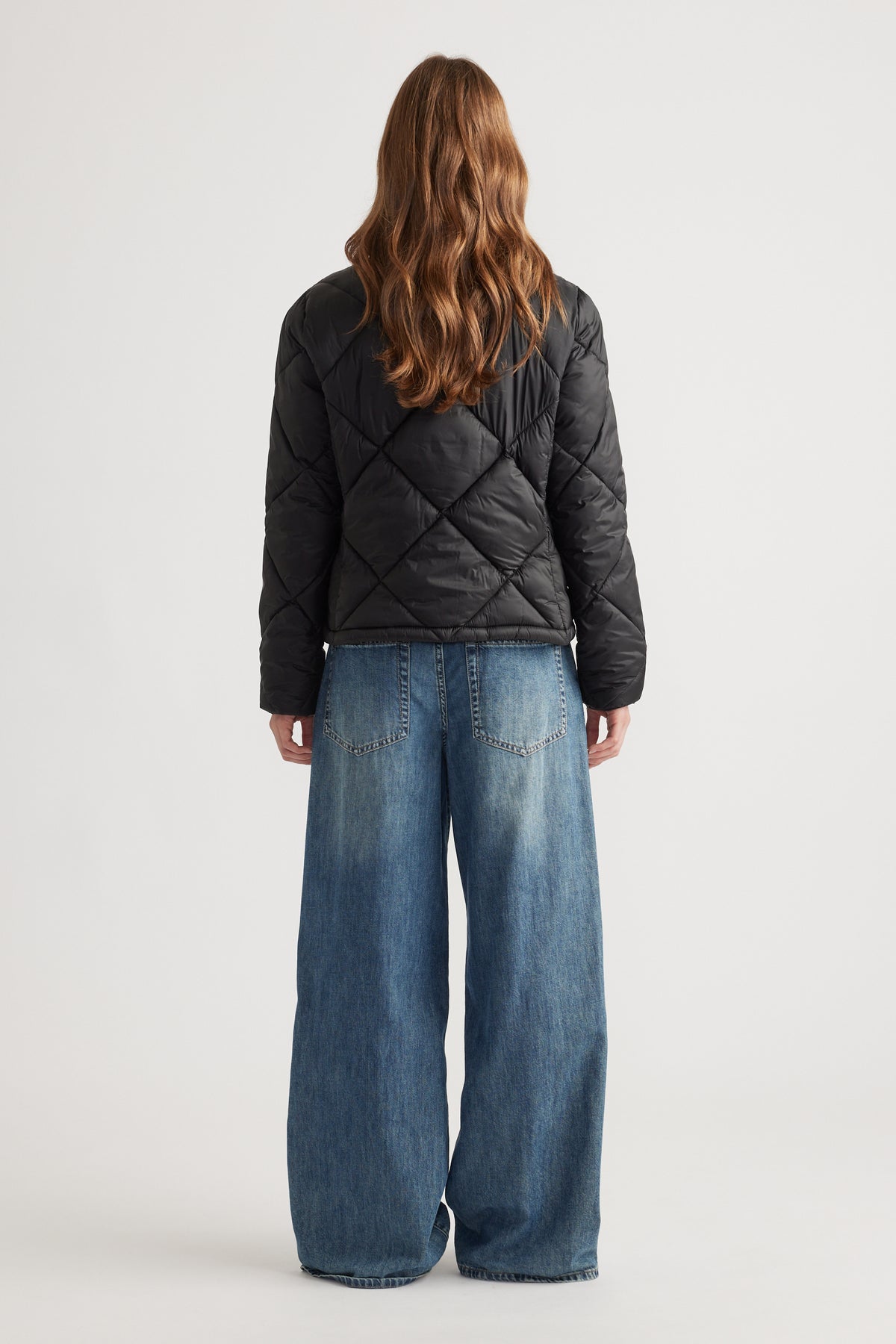 Woman shown from behind wearing a black quilted short puffer jacket with wide-leg blue jeans