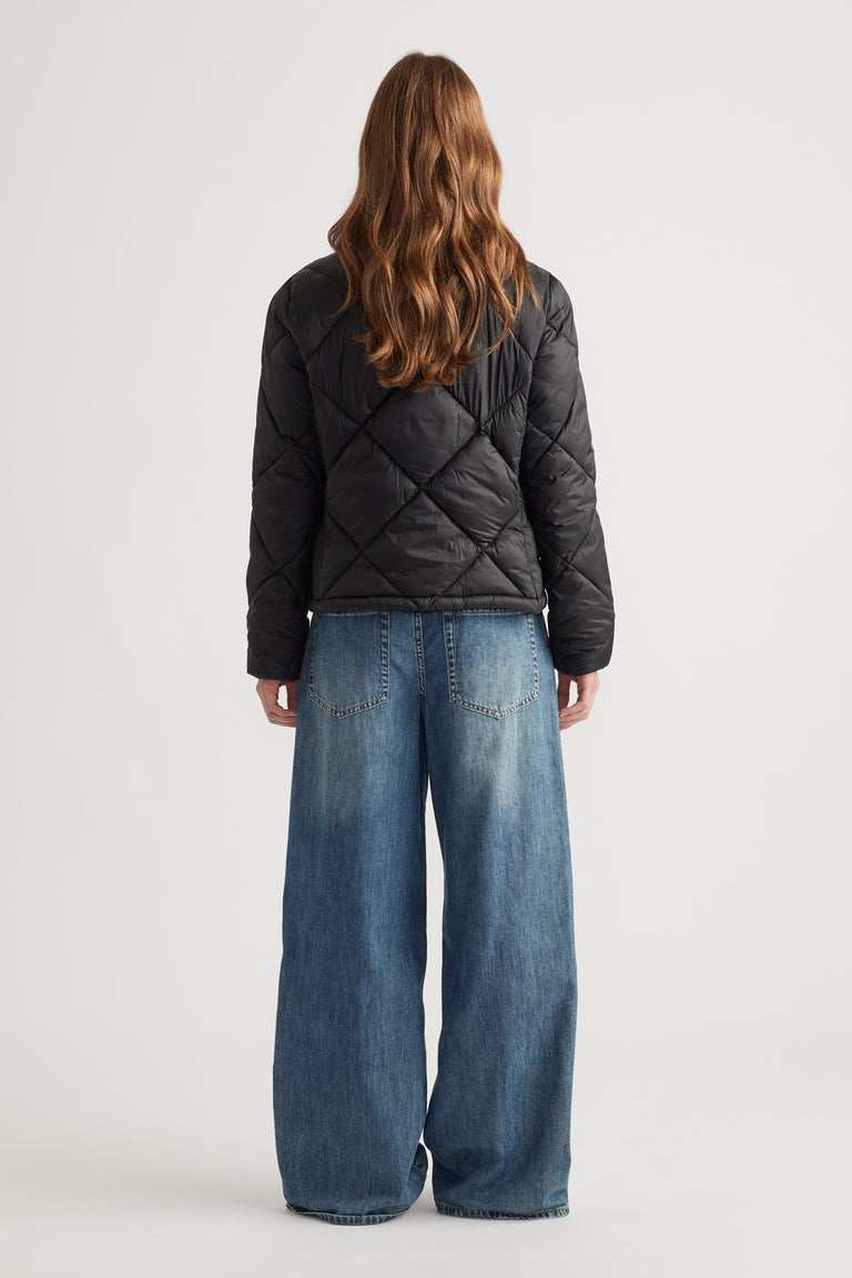 Woman shown from behind wearing a black quilted short puffer jacket with wide-leg blue jeans
