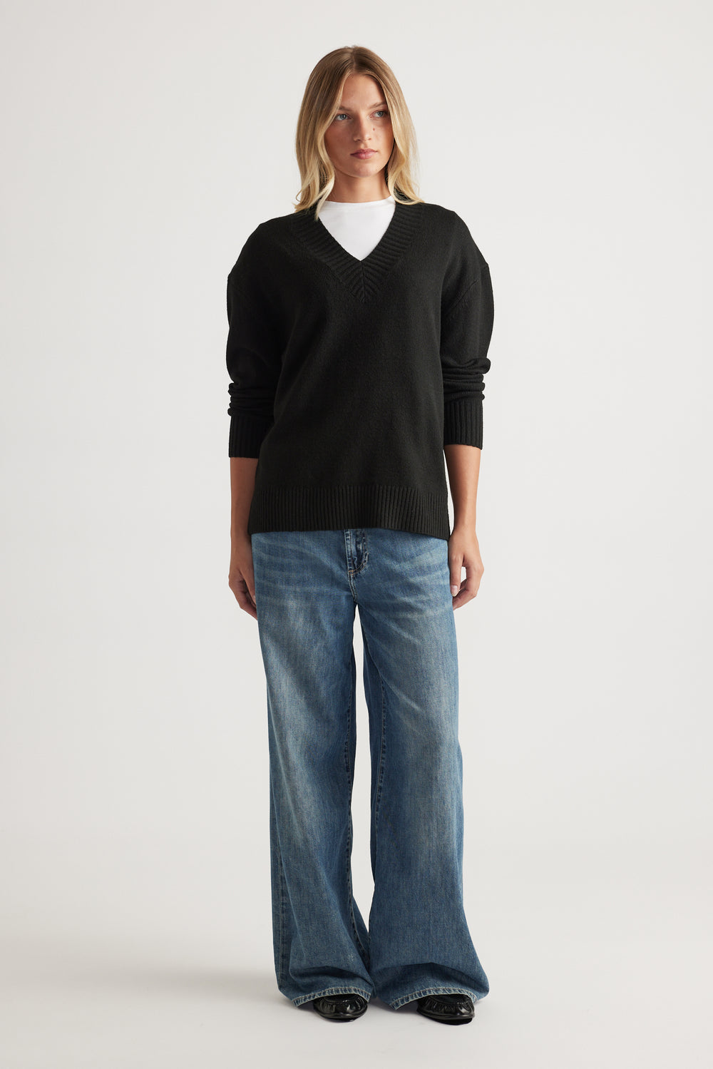 Woman wearing black V Neck Knit Jumper layered over white top with relaxed blue denim jeans by Decjuba Australian fashion brand
