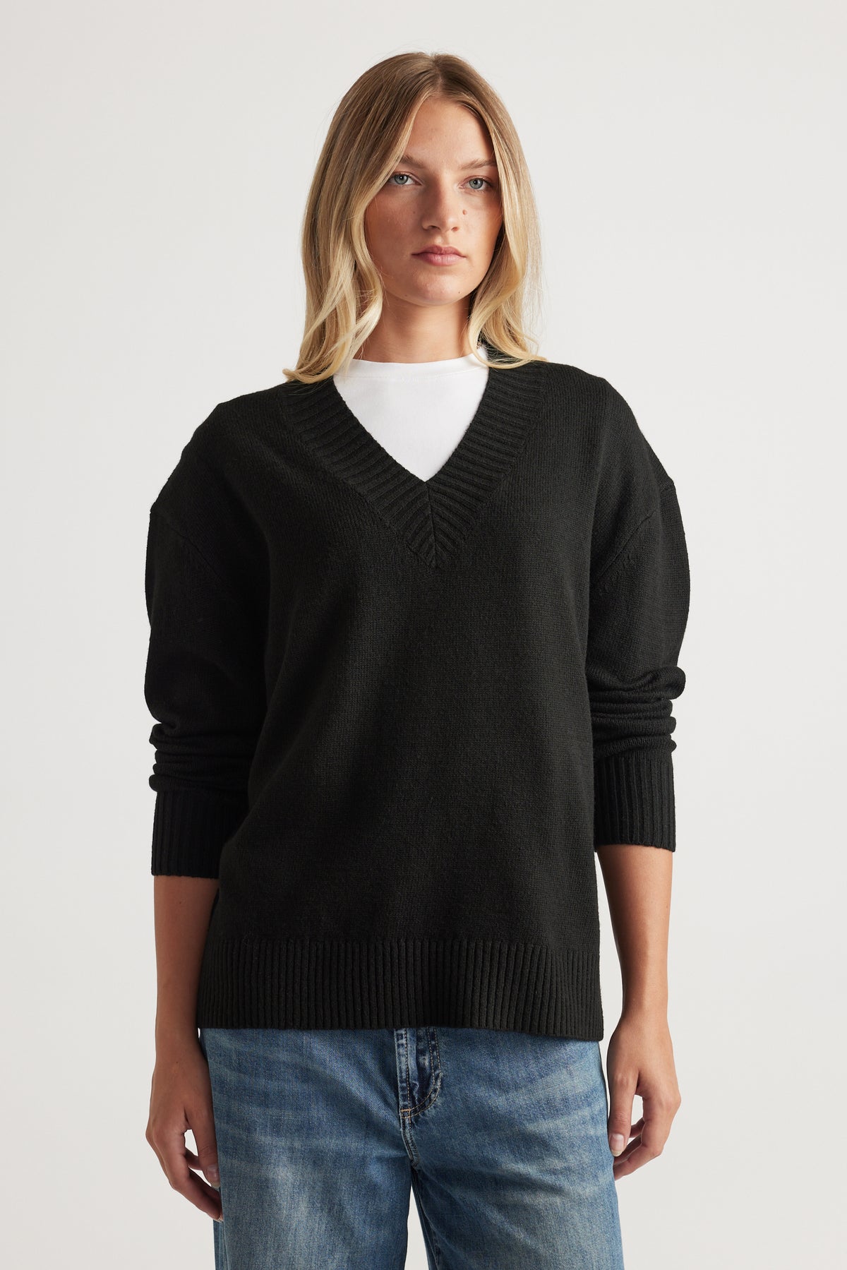 Woman wearing black V Neck Knit Jumper layered over white top with relaxed blue denim jeans by Decjuba Australian brand