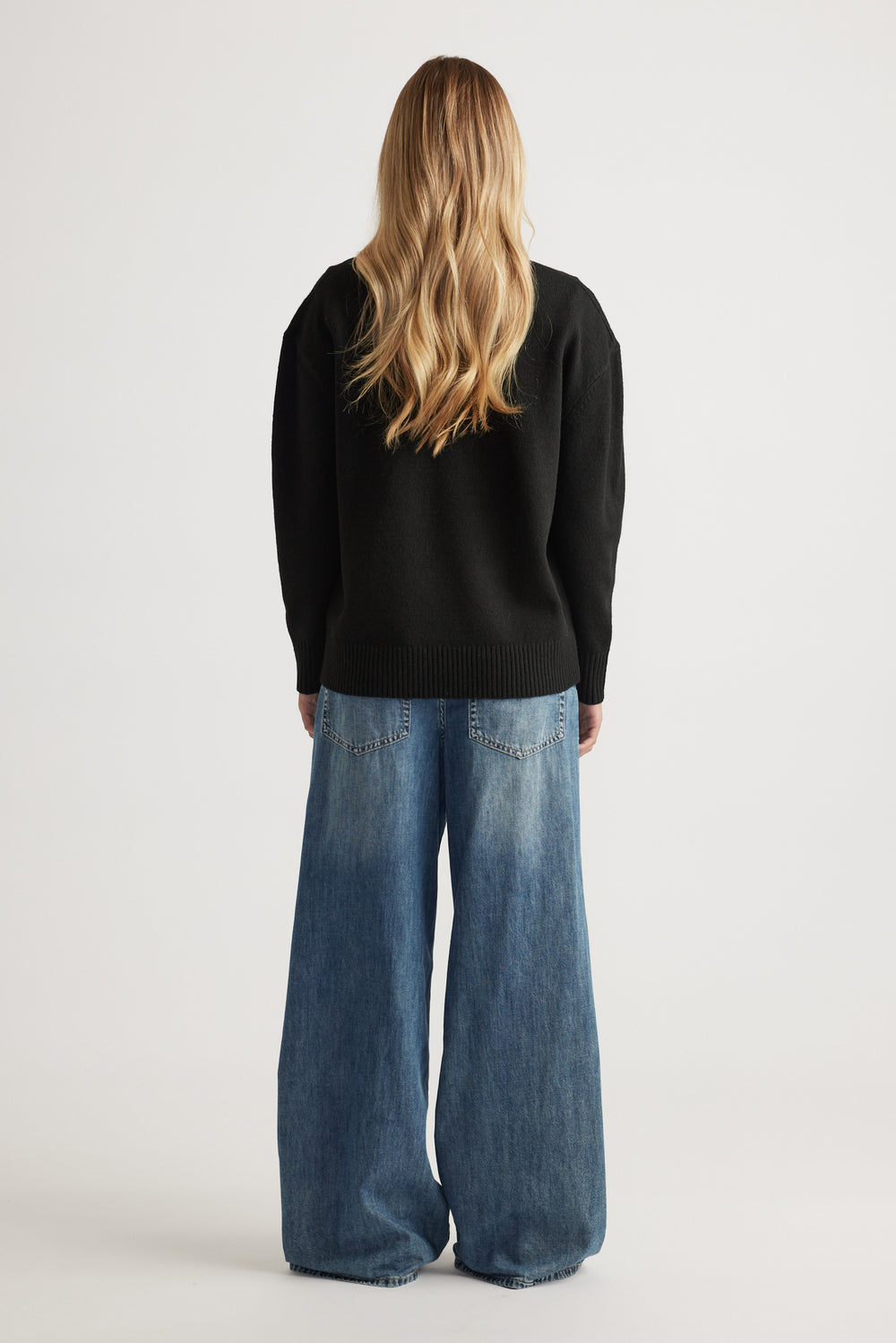 Back view of V Neck Knit Jumper in black paired with relaxed wide-leg denim jeans by Decjuba Australian fashion brand