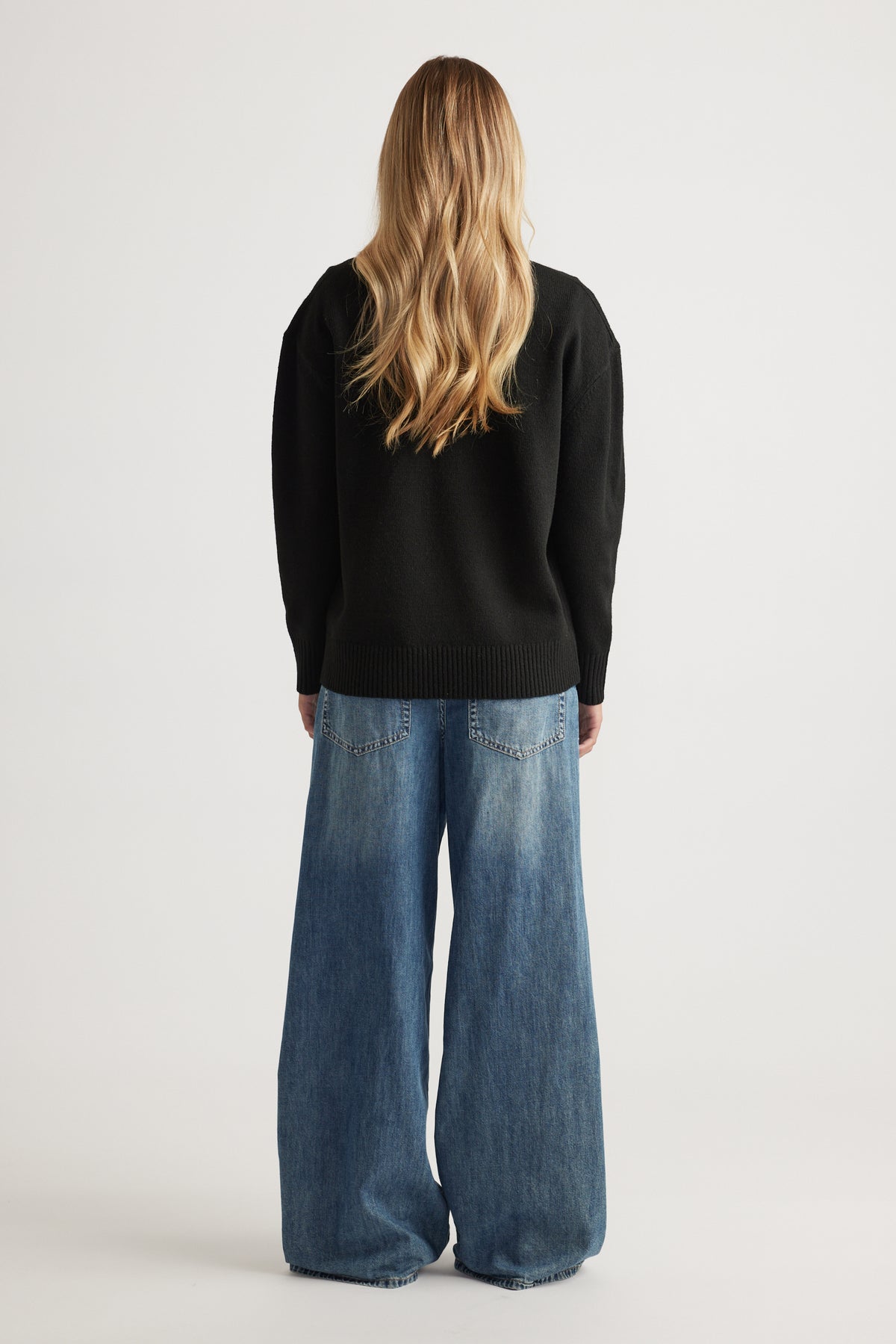Back view of V Neck Knit Jumper in black paired with relaxed wide-leg denim jeans by Decjuba Australian fashion brand