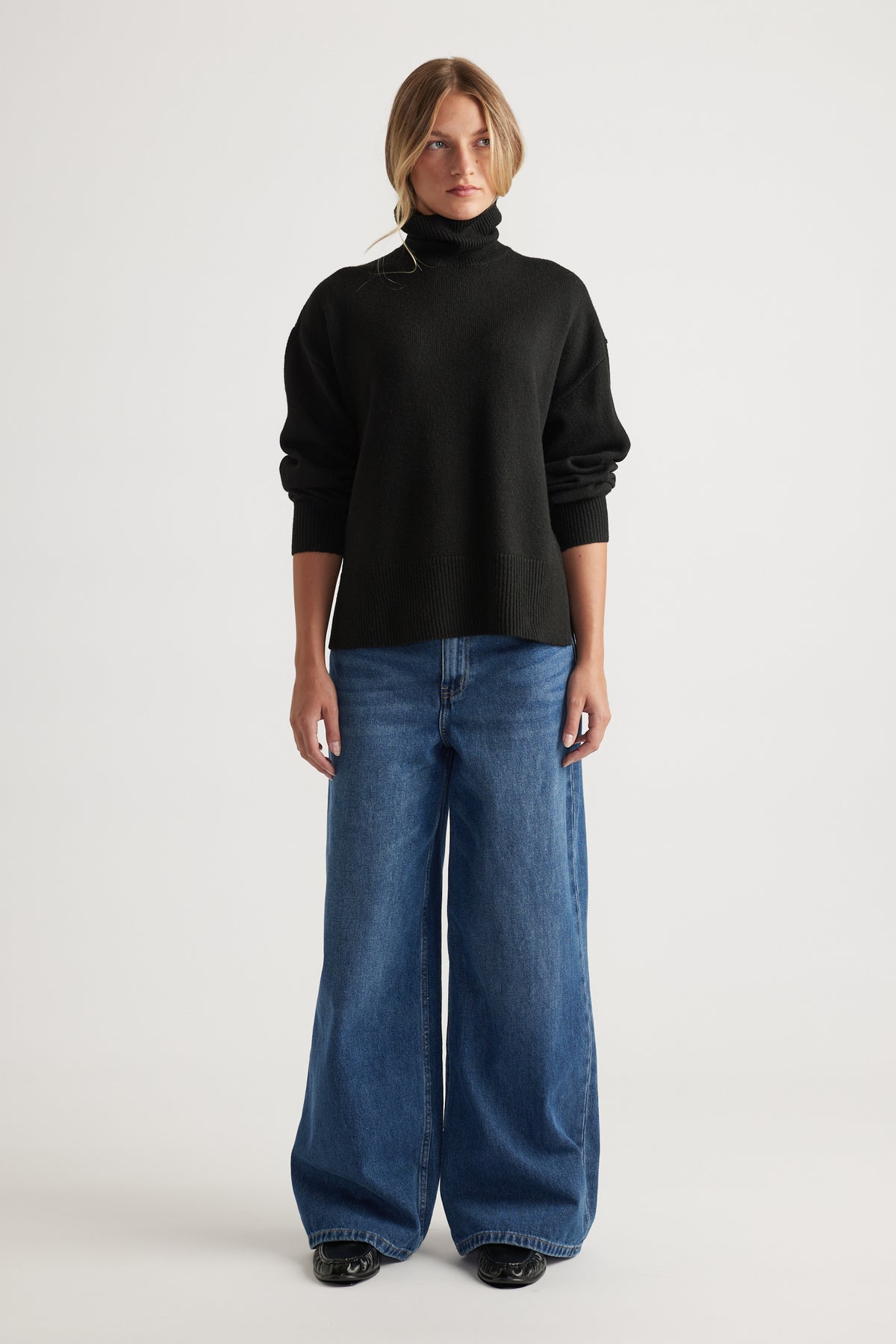 Woman wearing black Roll Neck Knit Jumper styled with wide-leg blue denim jeans by Decjuba Australian fashion brand