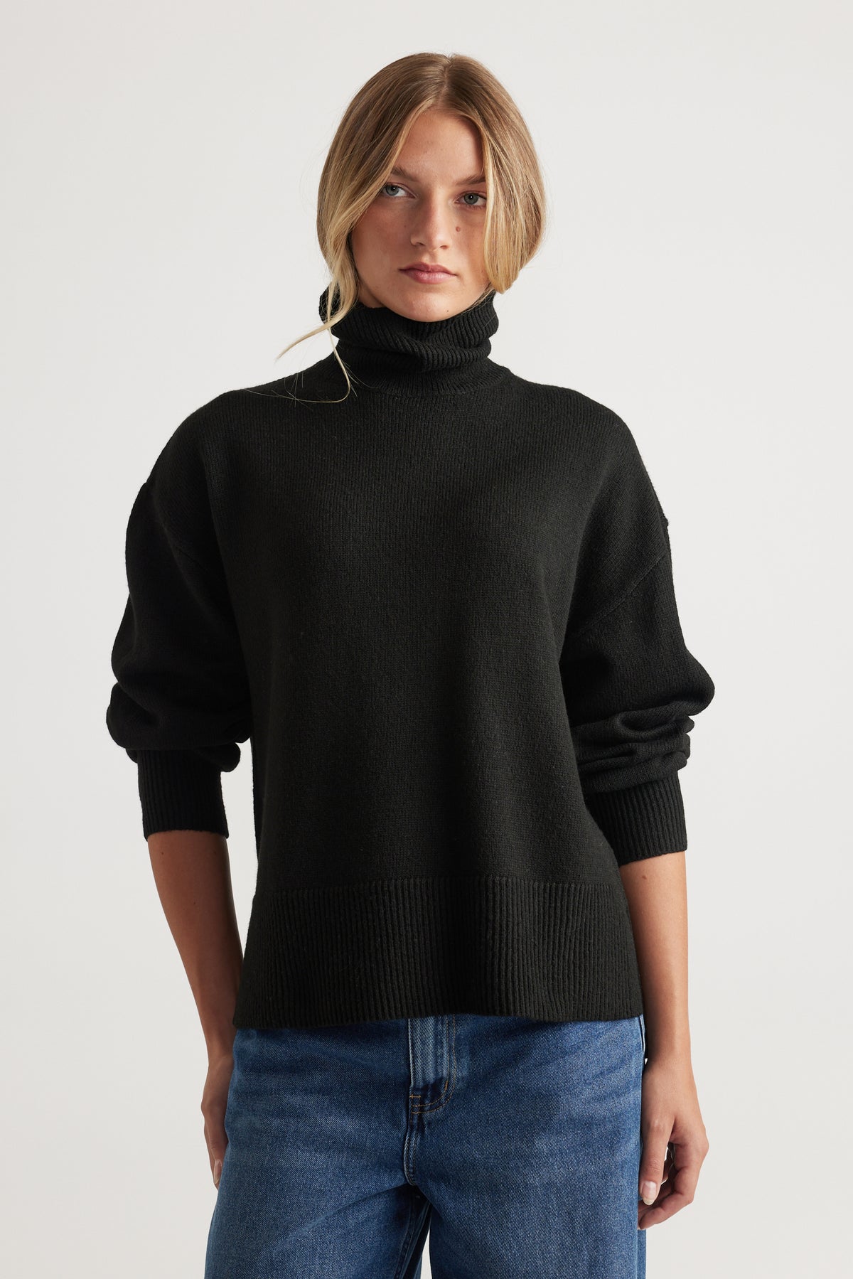 Woman wearing black Roll Neck Knit Jumper with ribbed cuffs and hem paired with blue denim jeans by Decjuba Australian fashion brand