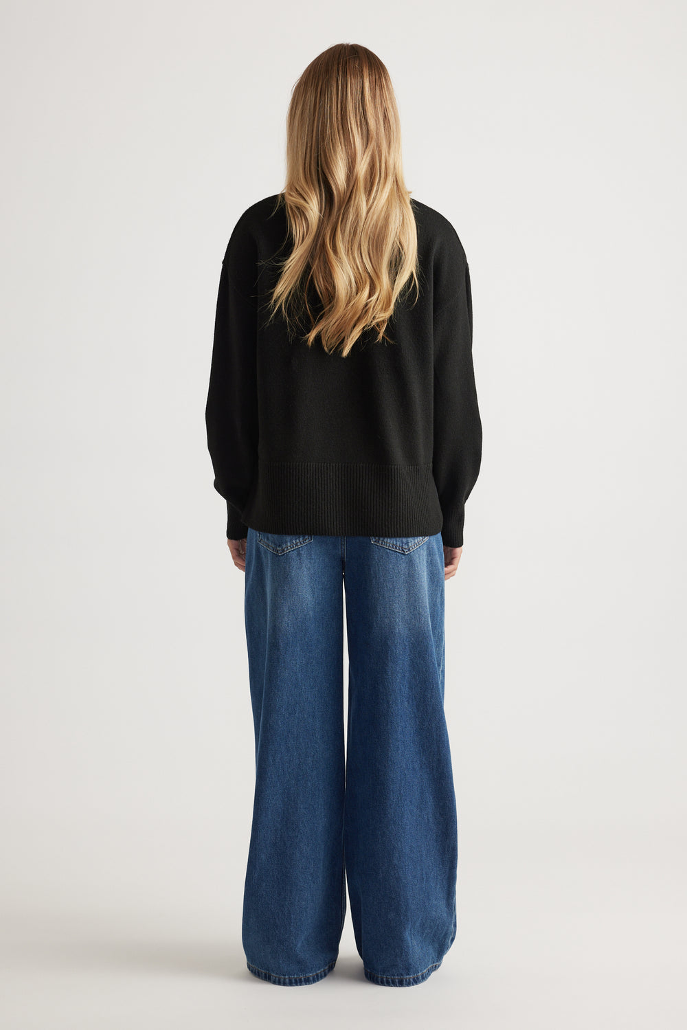 Back view of Roll Neck Knit Jumper in black knitwear paired with wide-leg blue denim jeans by Decjuba Australian brand
