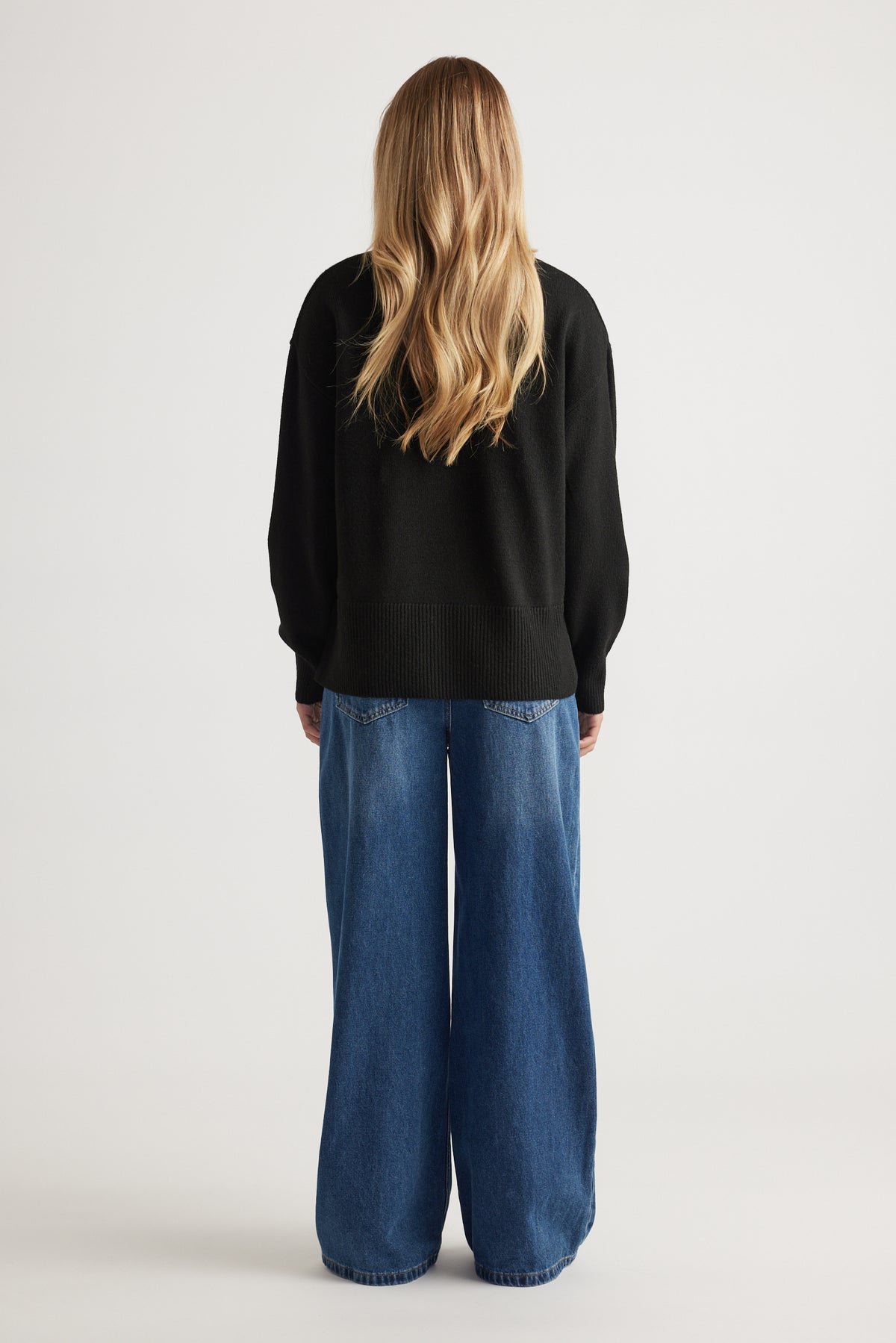 Back view of Roll Neck Knit Jumper in black knitwear paired with wide-leg blue denim jeans by Decjuba Australian brand