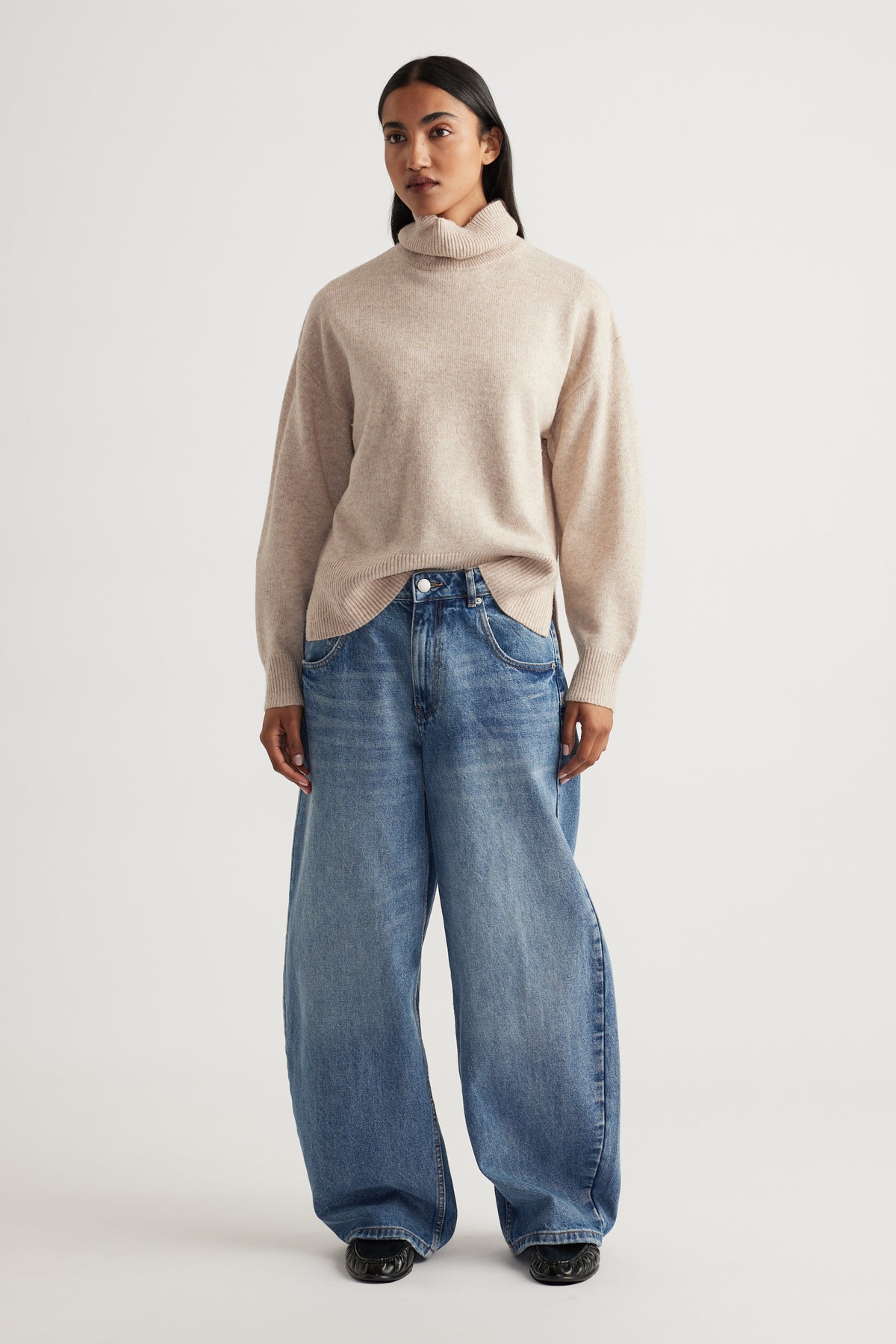 Woman modeling Roll Neck Knit Jumper in soft beige knitwear paired with relaxed wide-leg denim jeans by Decjuba Australian brand