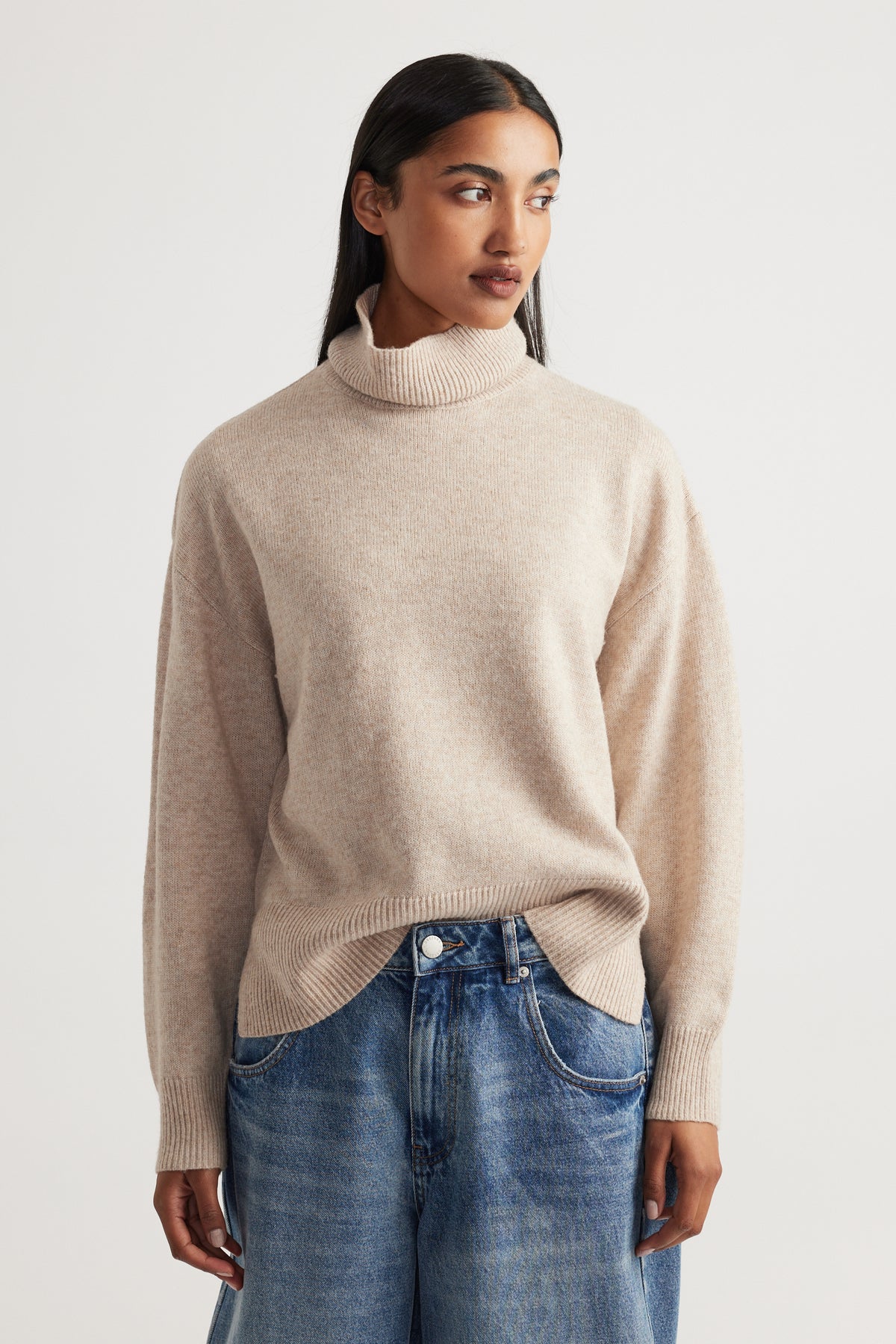 Woman wearing Roll Neck Knit Jumper in soft beige knitwear styled with relaxed blue denim jeans by Decjuba Australian brand