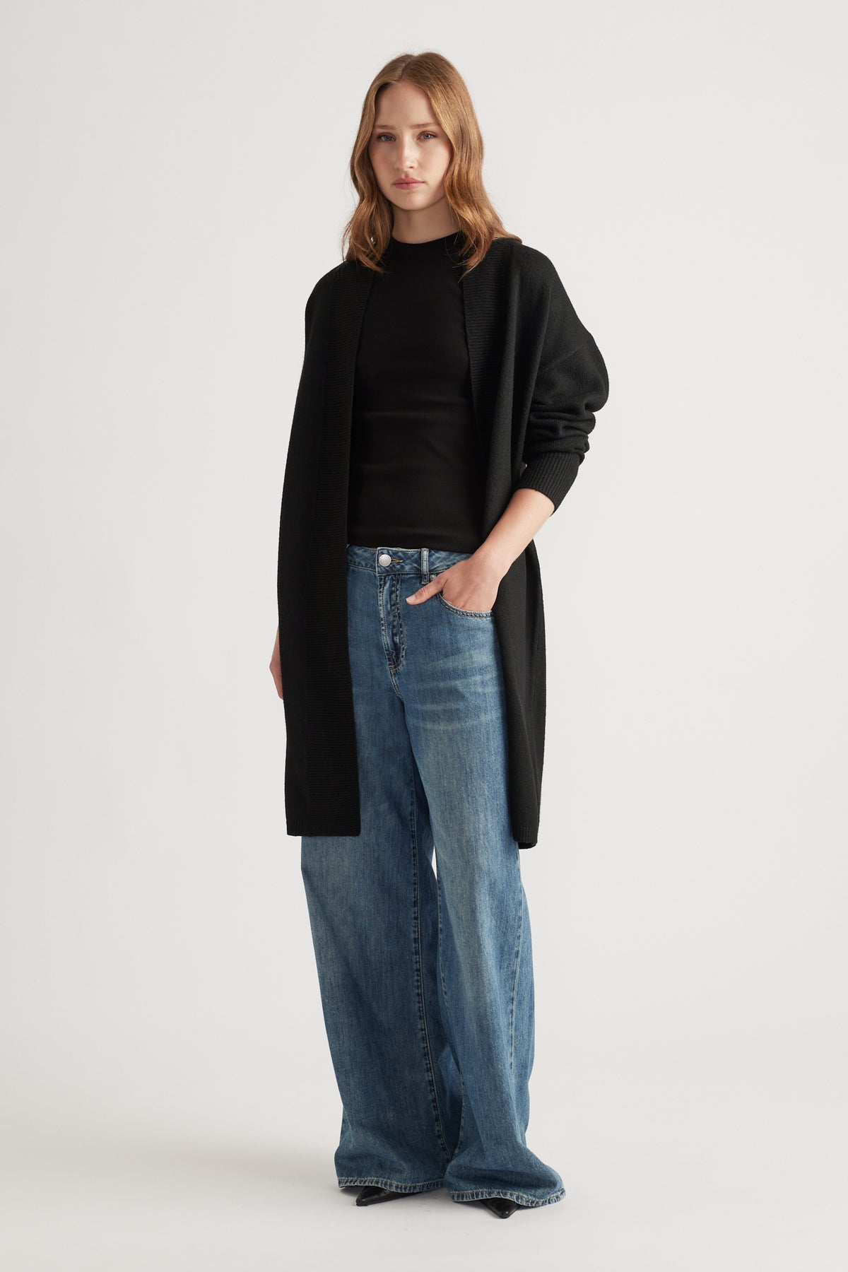 Woman wearing a loose black longline cardigan over a fitted black top paired with wide-leg light blue denim jeans
