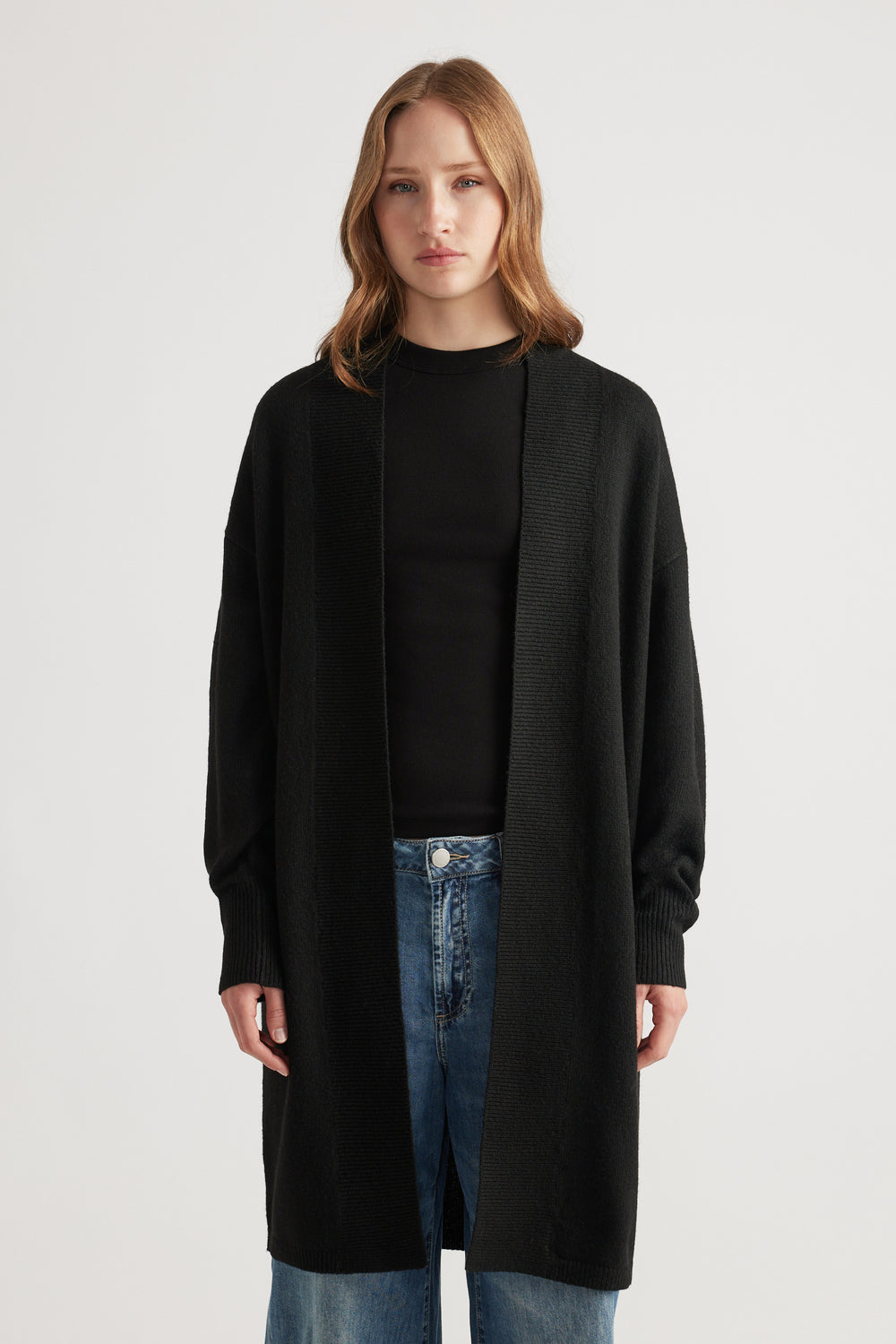 Woman wearing a relaxed black longline cardigan layered over a fitted black top paired with light blue denim jeans