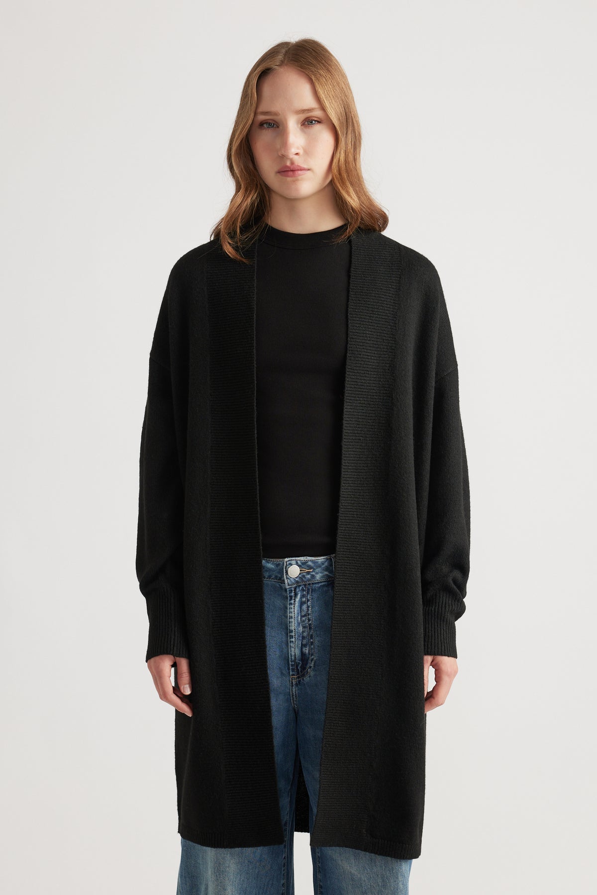Woman wearing a relaxed black longline cardigan layered over a fitted black top paired with light blue denim jeans