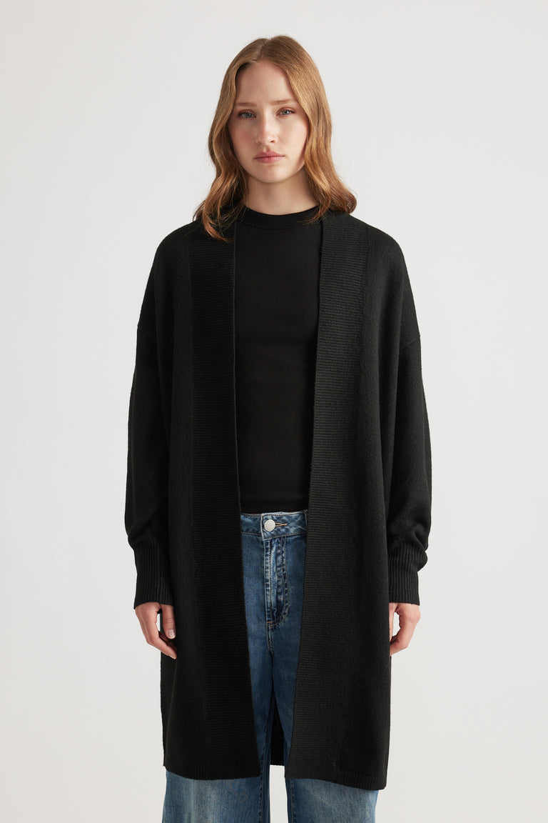 Woman wearing a relaxed black longline cardigan layered over a fitted black top paired with light blue denim jeans