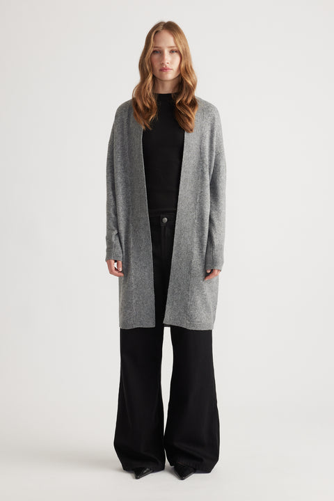Woman wearing mid-grey longline knit cardigan over black top and wide-leg black pants against white background