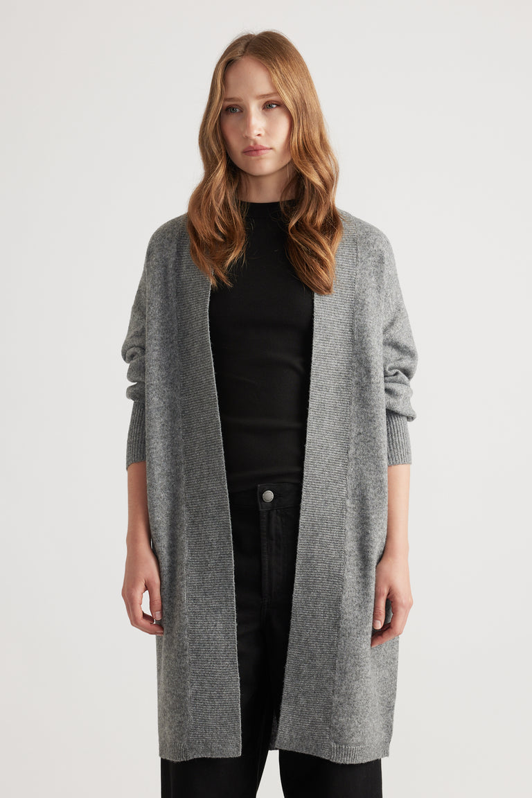 Model wearing a mid-grey longline knit cardigan layered over a fitted black top and black pants against a neutral background