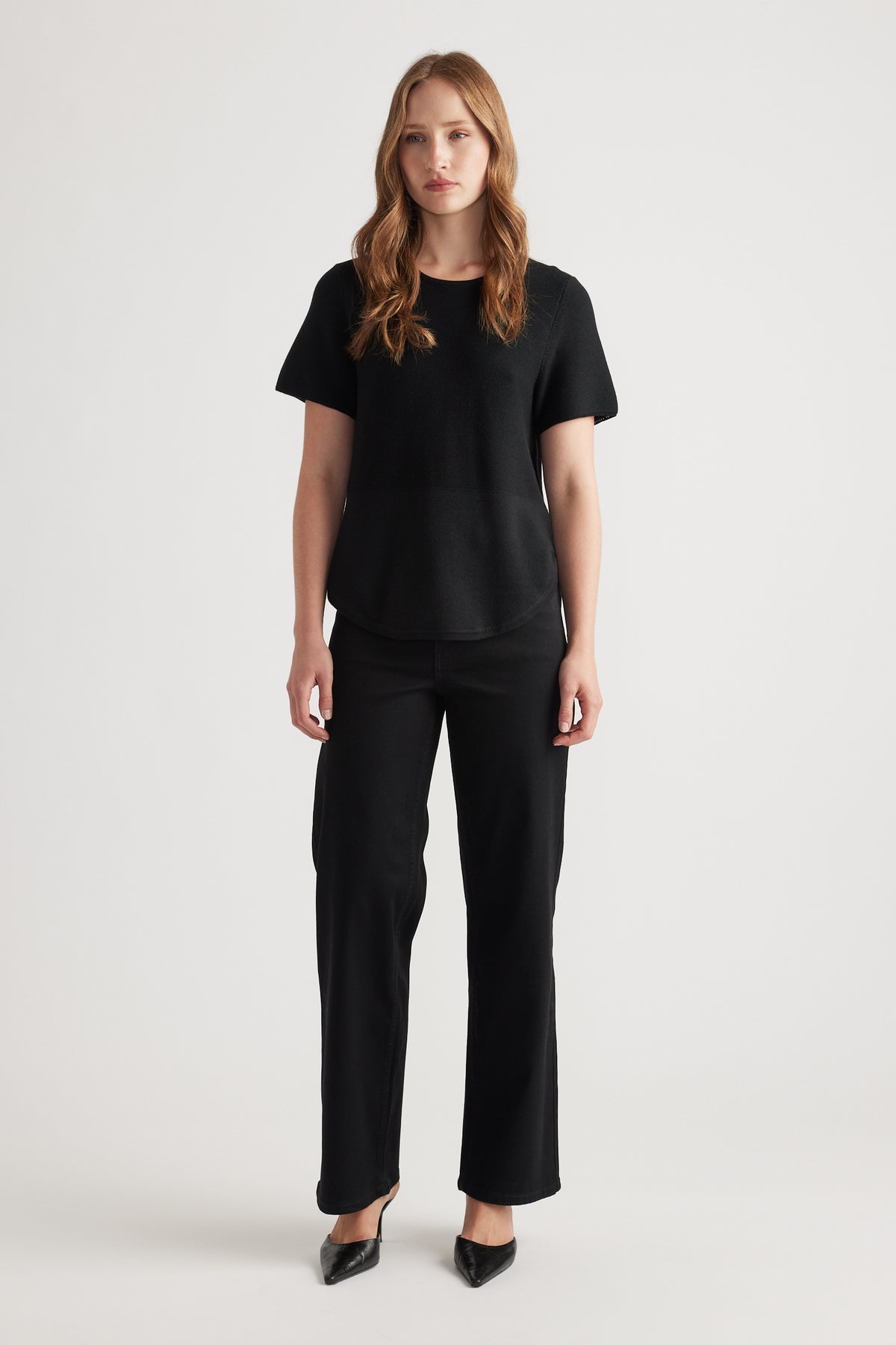 Woman wearing a black knitted short sleeve top paired with straight leg black pants and black pointed heels
