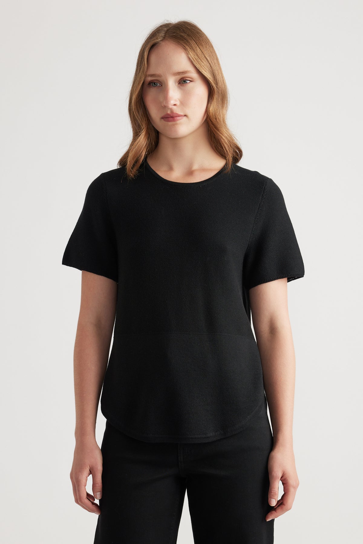 Woman wearing a fitted black knitted short sleeve top with a round neckline paired with black pants in a minimalist style