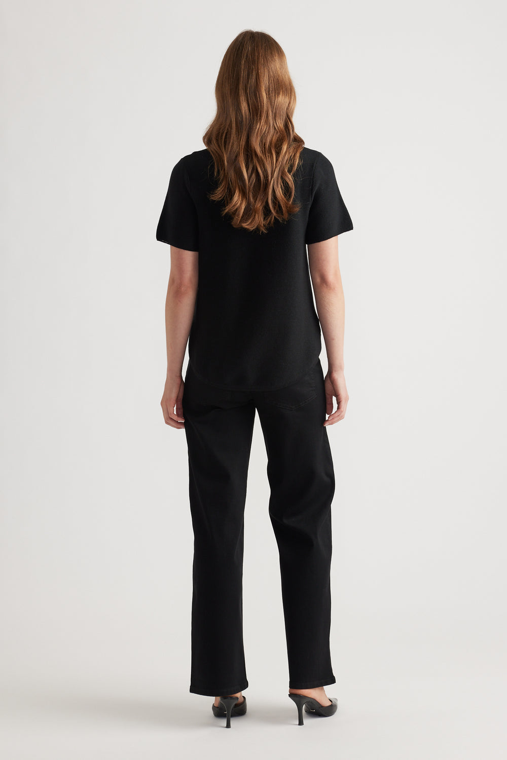 Woman wearing a relaxed black knitted short sleeve top paired with straight black pants and black heels from the back view