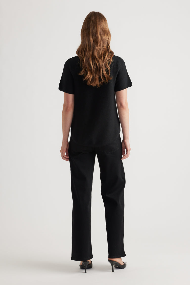 Woman wearing a relaxed black knitted short sleeve top paired with straight black pants and black heels from the back view