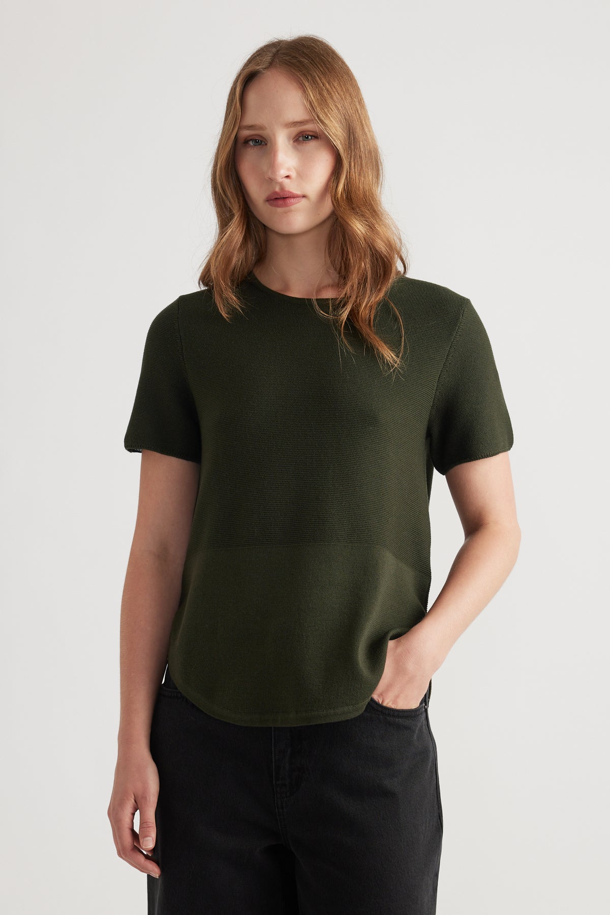 Woman wearing a forest green knitted short sleeve top paired with relaxed black jeans for a minimalist look