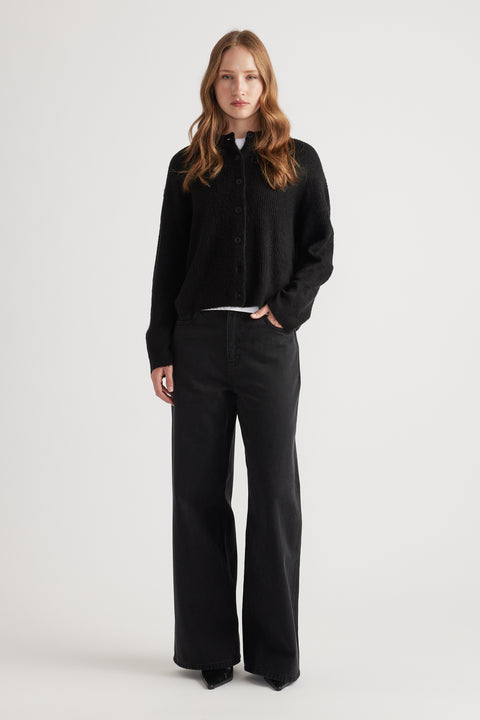 Woman wearing a relaxed black knit cardigan paired with wide-leg black denim jeans for a minimalist look
