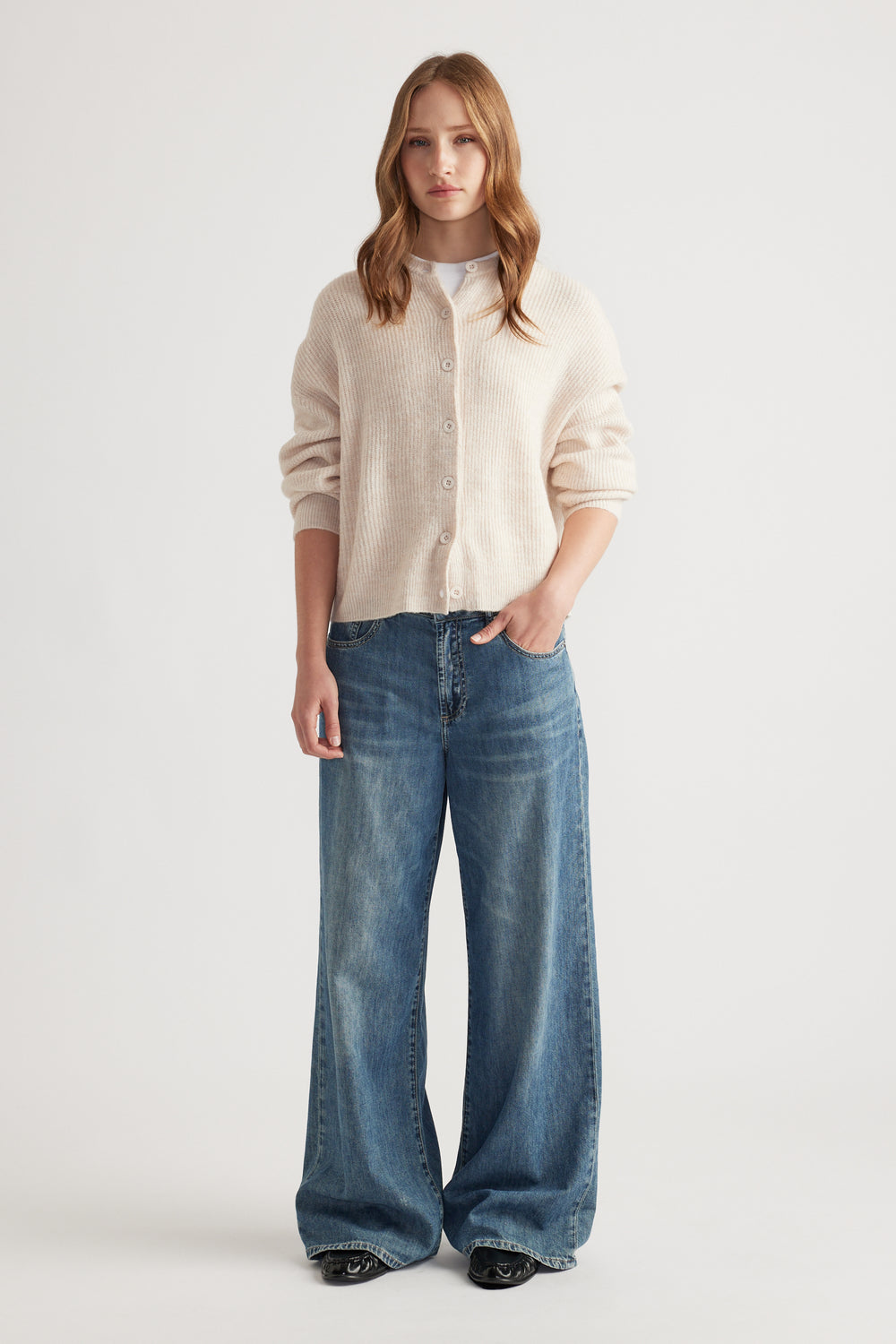 Woman wearing a soft cream knit cardigan layered over a white top, paired with wide-leg blue denim jeans for relaxed style