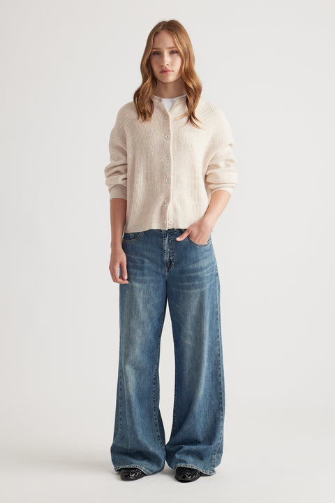 Woman wearing a soft cream knit cardigan layered over a white top, paired with wide-leg blue denim jeans for relaxed style
