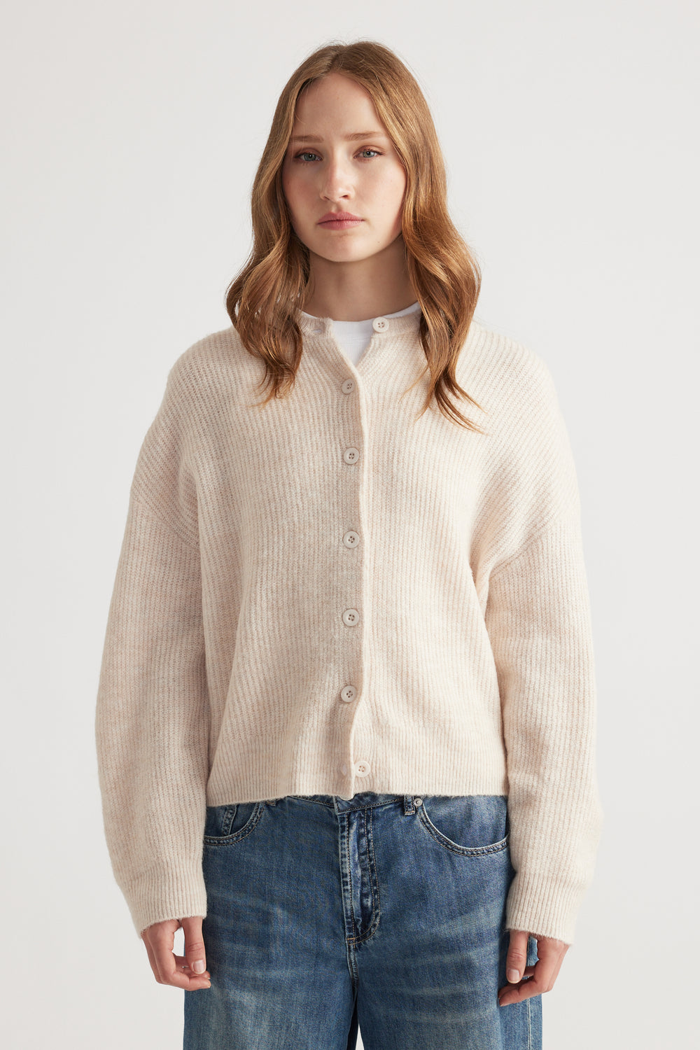 Woman wearing a soft neutral-toned knit cardigan with dropped shoulders paired with relaxed mid-blue denim jeans