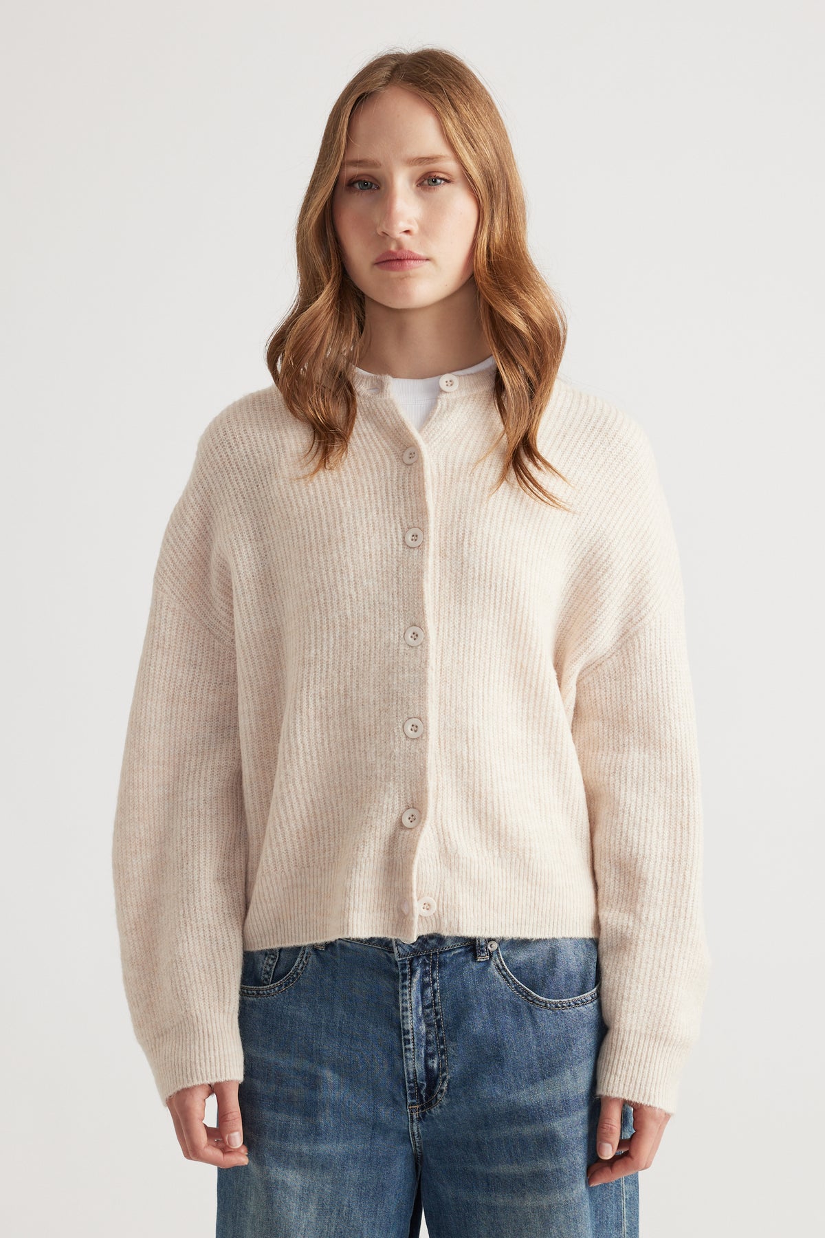 Woman wearing a soft neutral-toned knit cardigan with dropped shoulders paired with relaxed mid-blue denim jeans