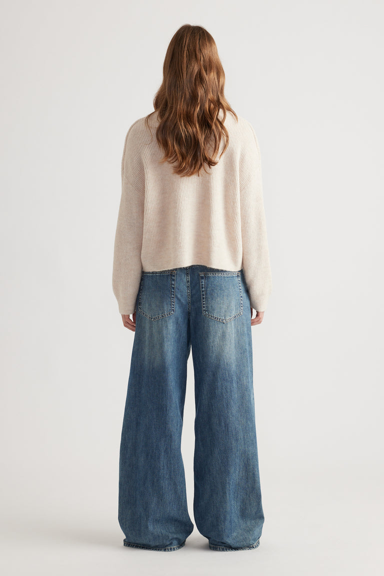 Woman with wavy hair wearing a cozy beige knit cardigan paired with relaxed wide-leg blue denim jeans from behind viewpoint