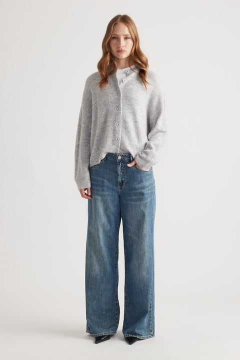 Young woman wearing a soft grey knit cardigan over a white top paired with relaxed wide-leg blue denim jeans and black shoes.