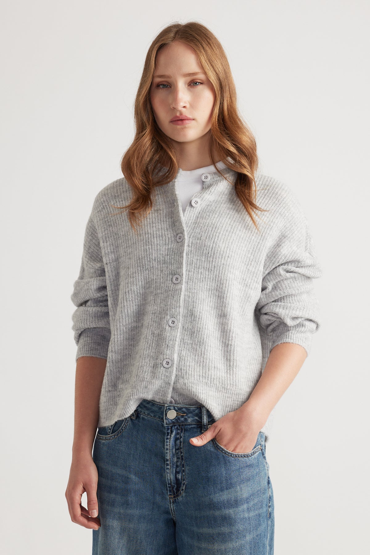 Young woman wearing a soft grey knit cardigan buttoned over a white top paired with relaxed fit blue jeans