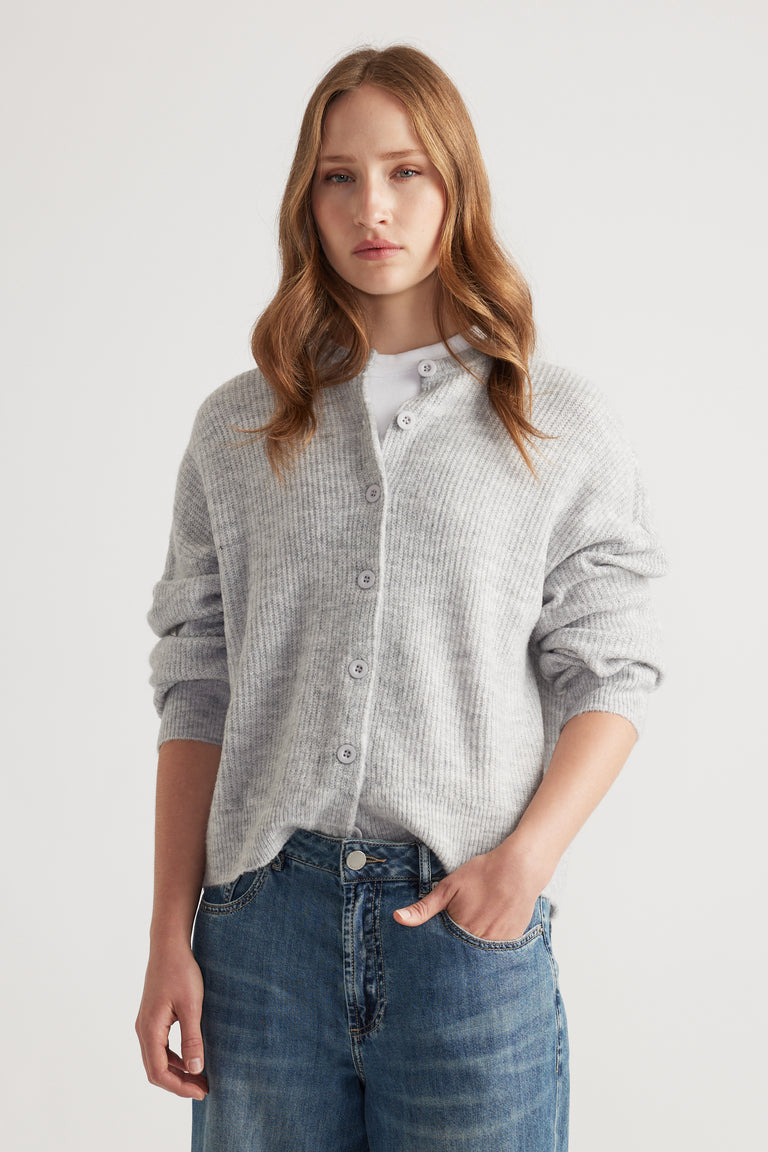 Young woman wearing a soft grey knit cardigan buttoned over a white top paired with relaxed fit blue jeans