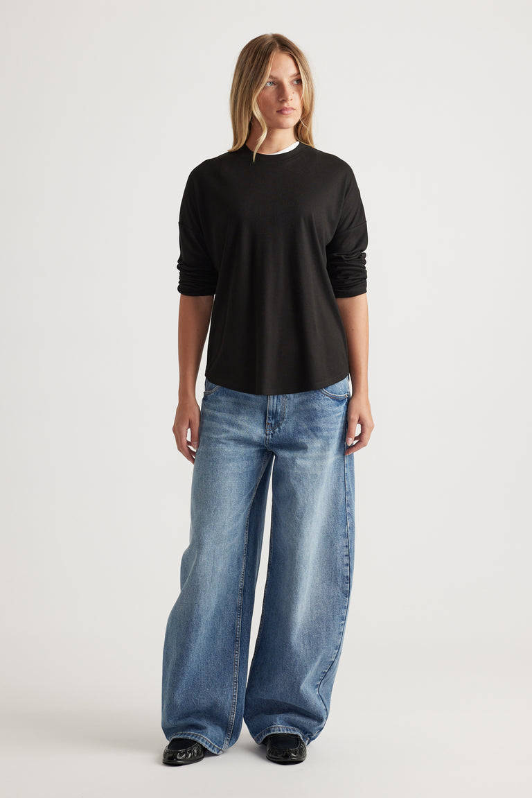 Woman wearing a black long sleeve rib top paired with loose light blue wide-leg jeans and black shoes