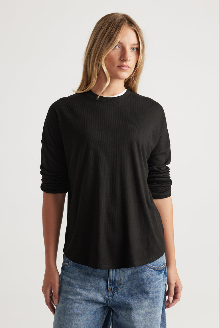 Woman wearing a relaxed-fit black long sleeve rib top paired with light wash blue jeans for a casual look
