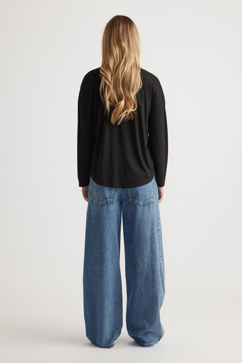 Woman seen from behind wearing a black long sleeve rib top paired with wide-leg light blue denim jeans