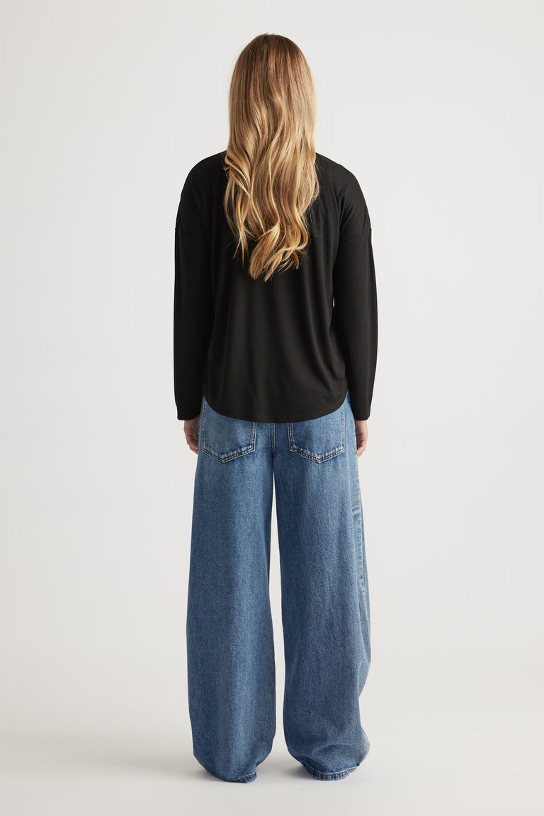 Woman seen from behind wearing a black long sleeve rib top paired with wide-leg light blue denim jeans